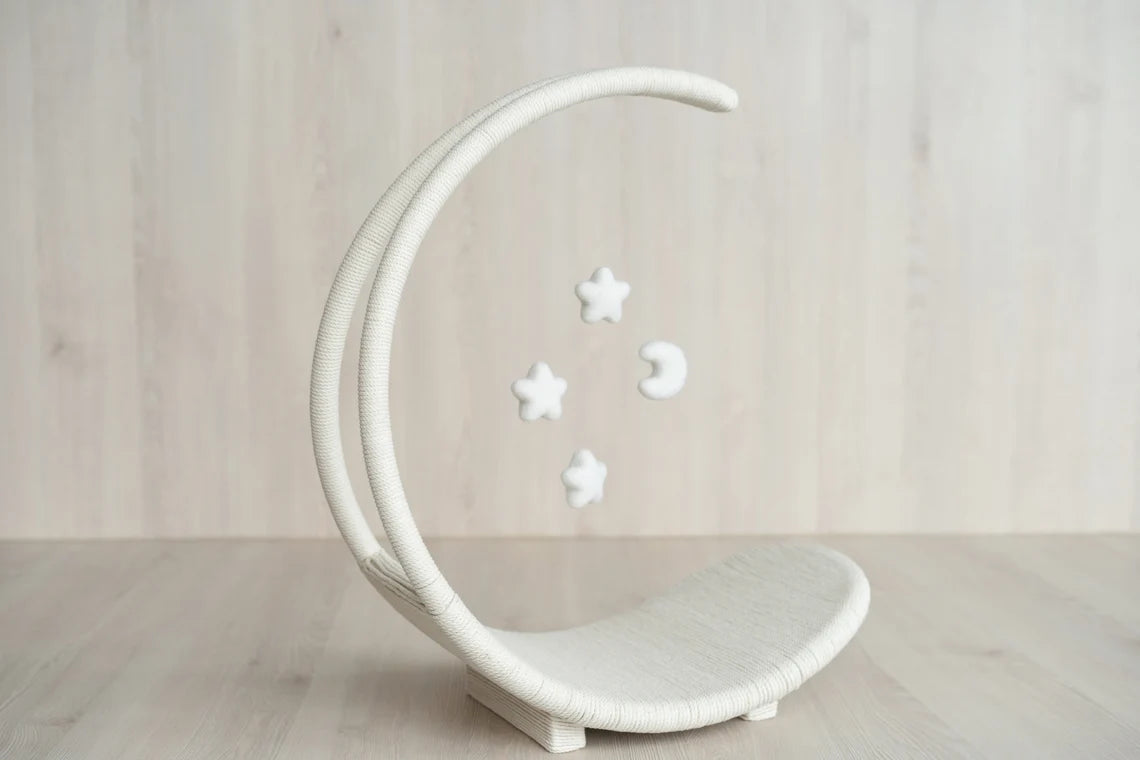 White crescent moon-shaped chair with decorative stars on a light wooden floor.
