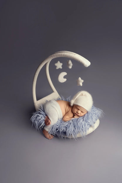 Newborn baby in a moon-shaped chair with star decorations on a dark background