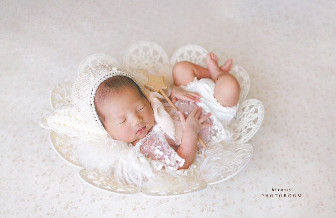 Newborn baby in a lace basket wearing a white bonnet on a light background