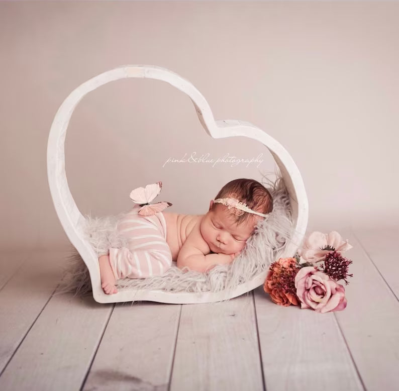 Newborn baby in a heart-shaped chair with flowers on a wooden floor